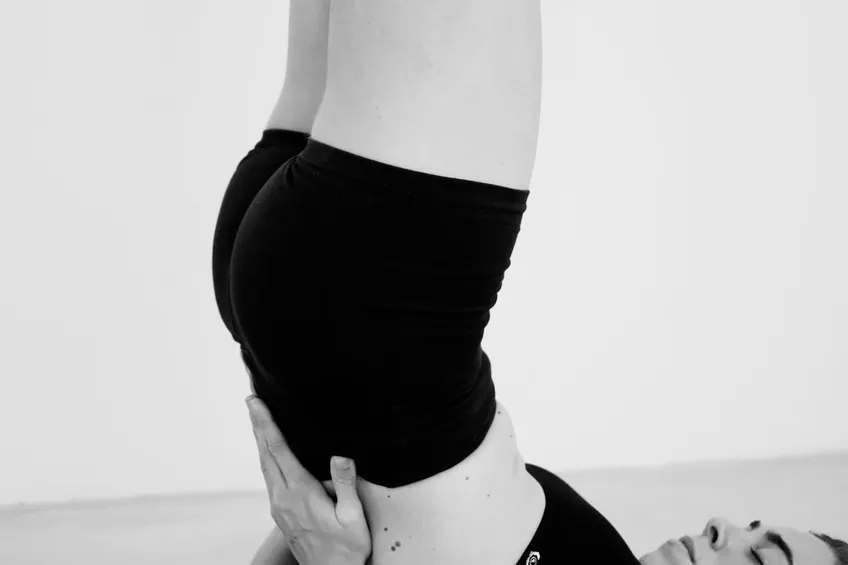 A student in shoulder stand, supported by their hands, in black and white